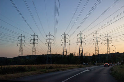 Electricity pylon by road against sky during sunset