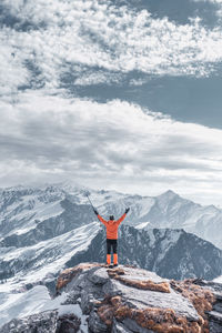 Rear view of man standing on cliff against snow capped mountain
