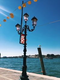 Low angle view of lantern hanging by sea against clear blue sky