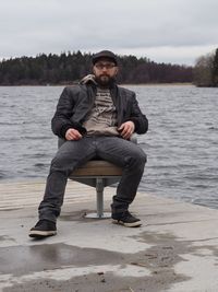 Full length portrait of young man sitting by lake