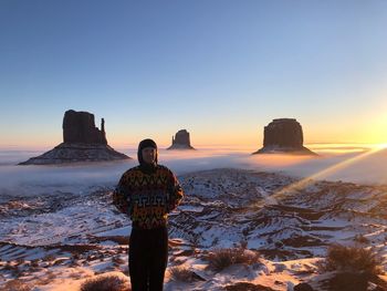 Portrait of man standing on snow covered land against sky during sunset