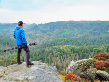 Photographer with folded tripod on end of cliff think. natural landscape in beautiful valley below