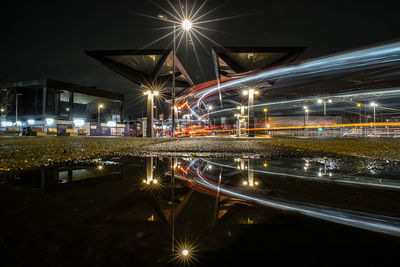 Light trails on illuminated street against sky at night