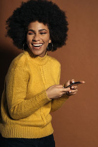 Smiling young woman using mobile phone against brown background