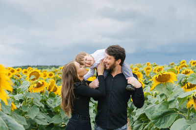 Cheerful loving young family with their son on vacation in a field with sunflowers