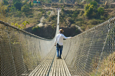 Rear view young man on rope bridge