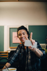 Portrait of smiling businessman with mobile phone showing peace sign while having food at table