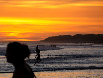 Silhouette people on beach against sky during sunset