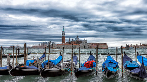 Boats in harbor against cloudy sky