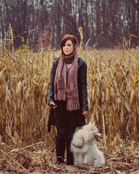 Full length portrait of beautiful woman with dog standing on dry corn field during winter