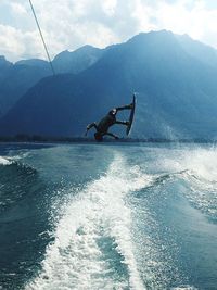 Man surfing in sea against mountains