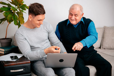 Young man with grandfather using laptop on sofa