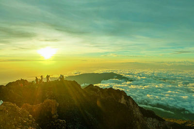 People on rocky mountain against sky during sunset