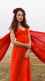 Portrait of woman in red dress standing against sky