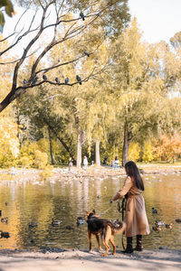 Woman with dog on riverbank against trees