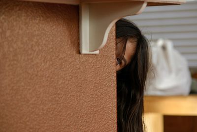 Close-up of girl peaking by wall