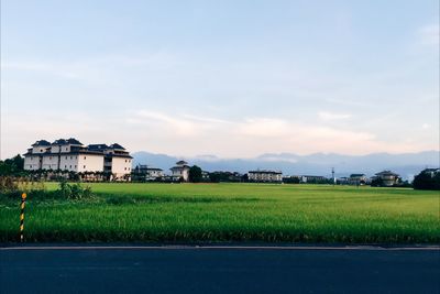 House on field by houses against sky