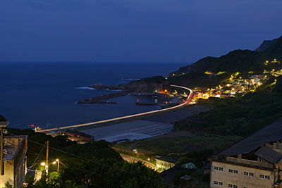 High angle view of illuminated city by sea against sky at night