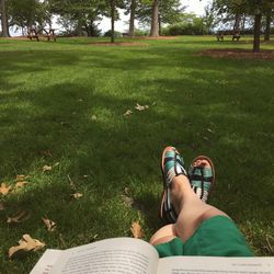 Low section of woman with book relaxing on grassy field in park