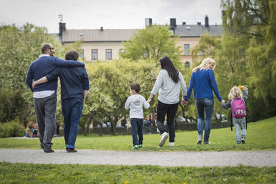 Rear view of female homosexual family walking at park with gay couple in background