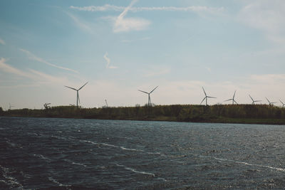 Windmills by lake against sky