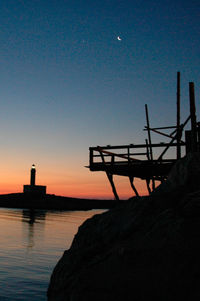 Silhouette built structure by sea against clear sky