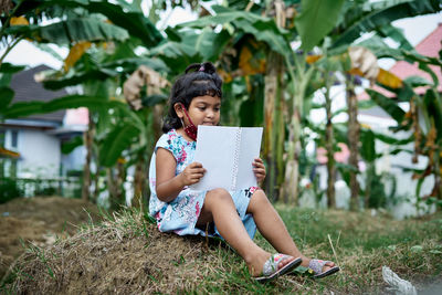 Full length of girl reading book while sitting outdoors