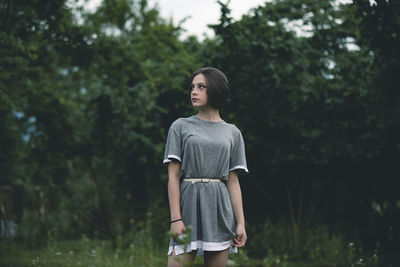 Woman looking away while standing against trees