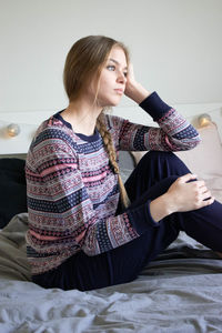 Young woman looking away while sitting on bed at home