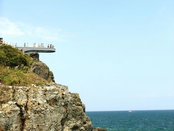 Low angle view of people at observation point over cliff in sea against sky