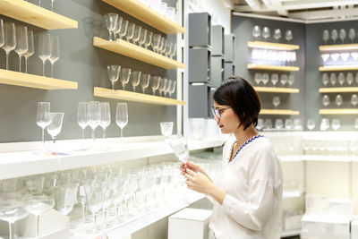 Asian young short hair beautiful woman choosing wine glasses to buy at furnishings glasses store