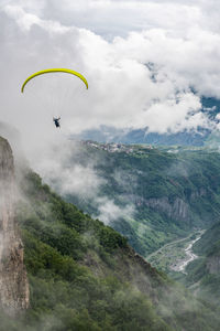 Person paragliding over mountains against sky