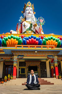Young man meditating in front of buddhist colorful goddess statue with blue sky at morning