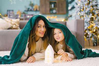 Beautiful family mom and daughter are covered with a blanket and look at the house with lights