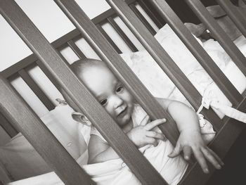 Close-up of baby boy looking through railing while lying in crib