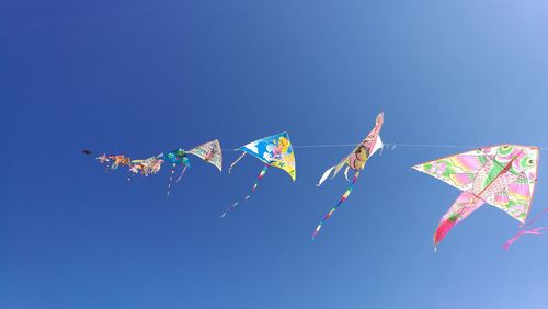 Low angle view of kites against clear blue sky