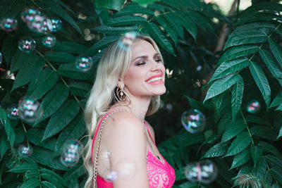 Close-up of bubbles by smiling woman standing against plants