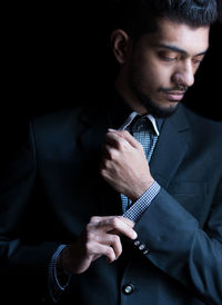 Handsome businessman adjusting sleeve against black background