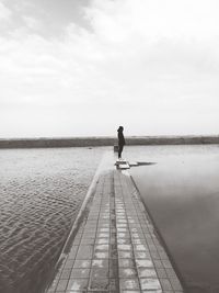 Man standing on jetty over sea against sky