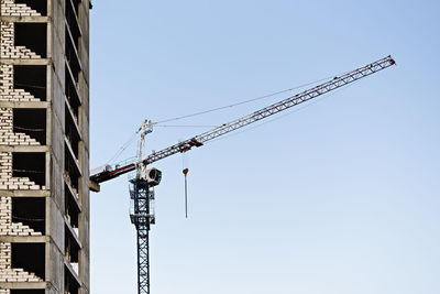 Low angle view of crane by building against sky