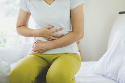 Midsection of woman with stomachache kneeling on bed at home