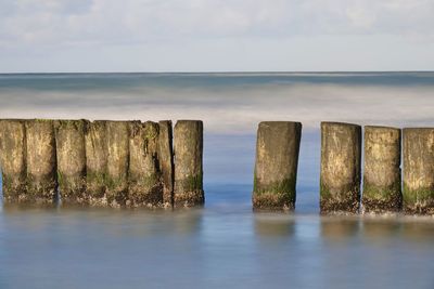 Wooden posts in sea against sky