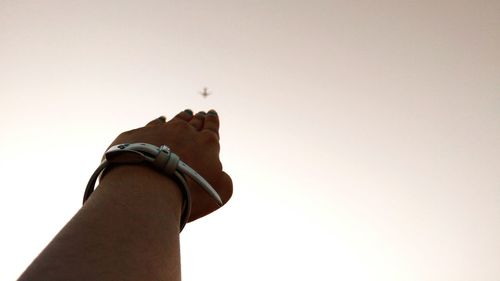 Cropped woman hand pointing at airplane against sky