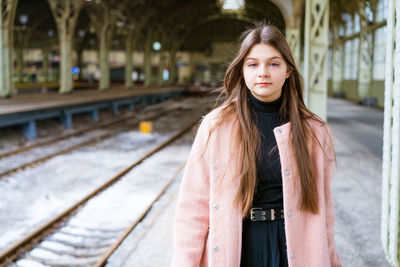 Beautiful young casual tourist woman with a suitcase in a pink coat waiting