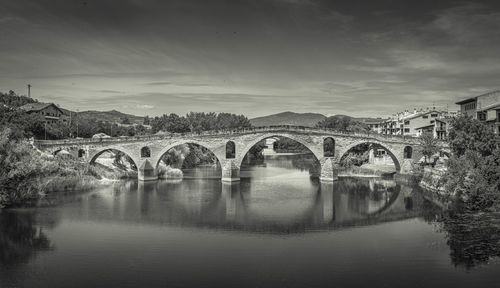 Arch bridge over river by buildings against sky