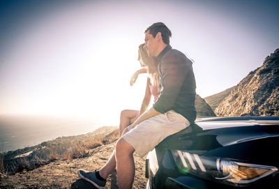 Full length of man sitting on car against sky