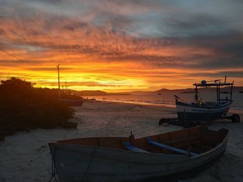 Boat moored on beach against sky during sunset