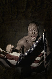 Angry senior man with american flag screaming while standing in room