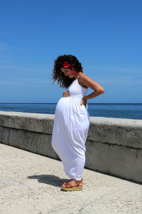 Full length of woman standing smiling down at her pregnant belly 