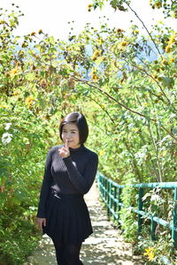 Portrait of young woman with finger on lips standing against plants